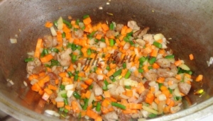 К обжаренному мясу добавляем лук, морковь и стрелки